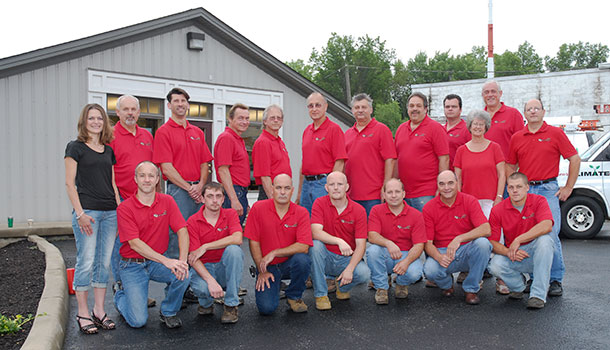 A group of people all wearing red shirts and jeans standing in front of a gray building